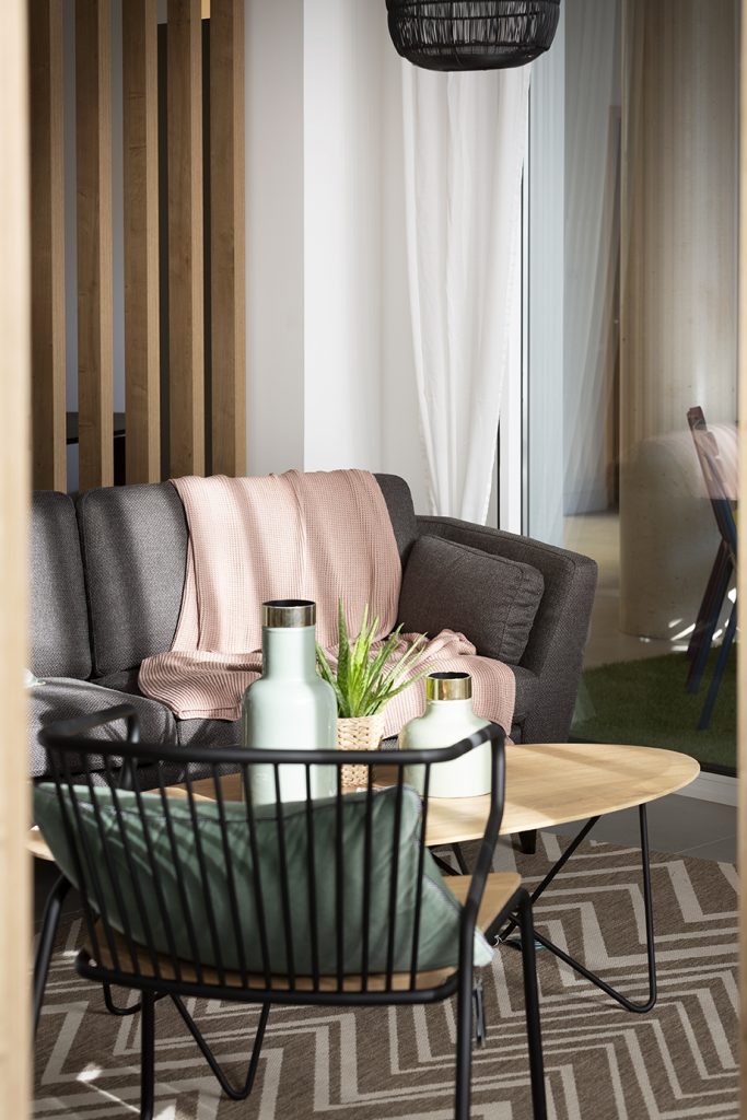 salon avec canapé gris plaid rose table basse en bois chaise en fer noir et tapis blanc et beige